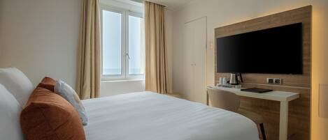A hotel room with a large bed, a desk with a flat-screen TV, and a window with curtains.