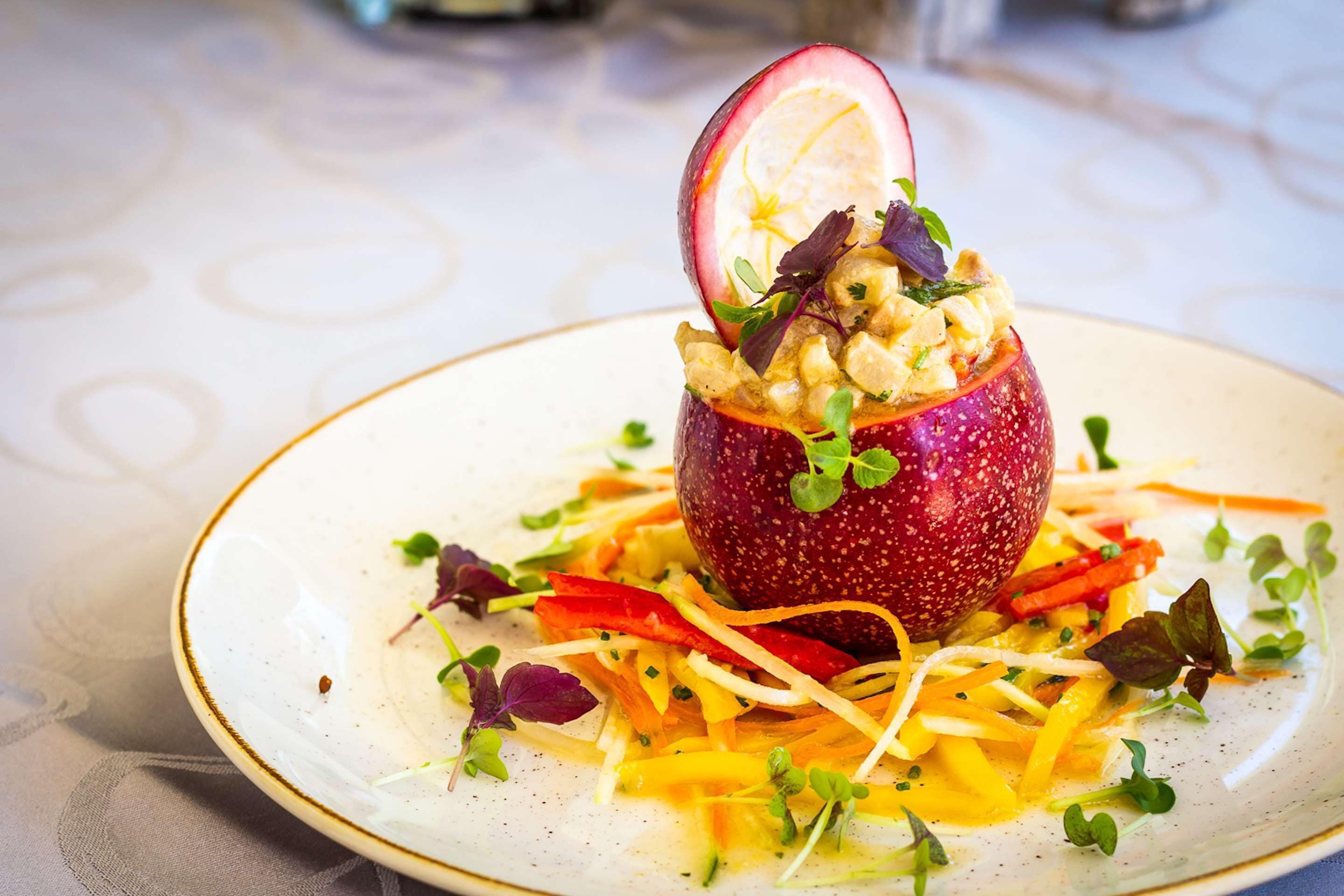 A plate with a red fruit-based dish, garnished with greens and thinly sliced vegetables.
