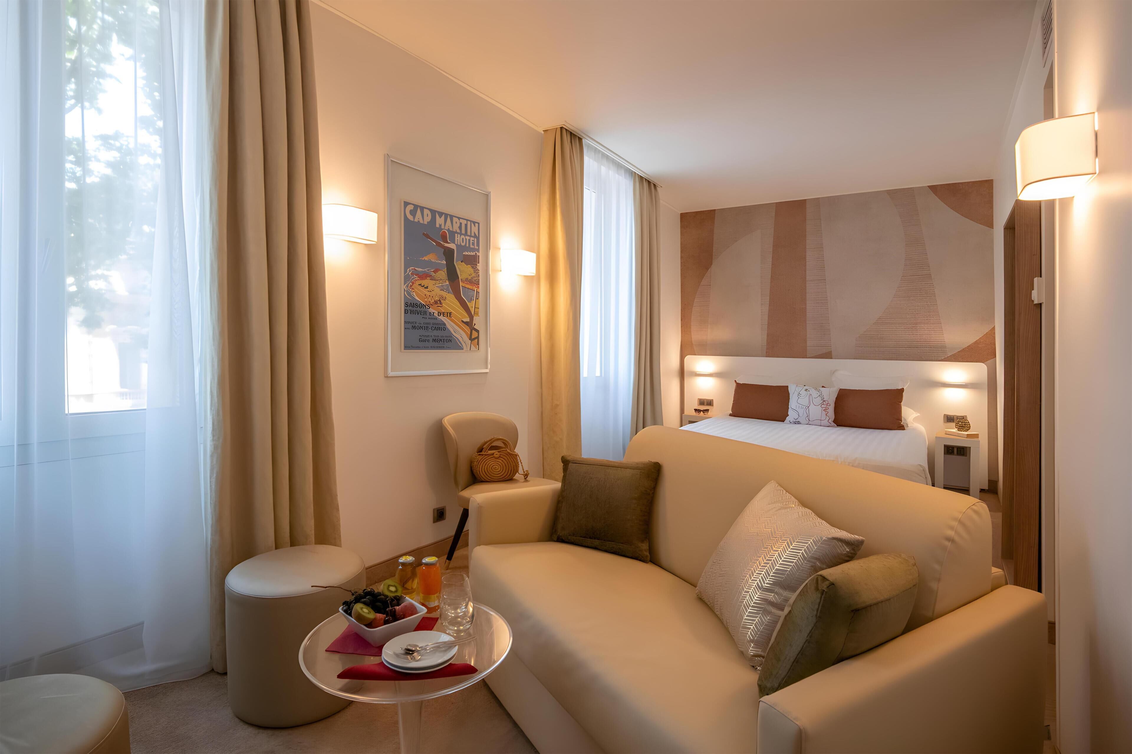 Een hotelkamer met een bed, een bank, een tafeltje met ontbijtartikelen en een poster aan de muur.