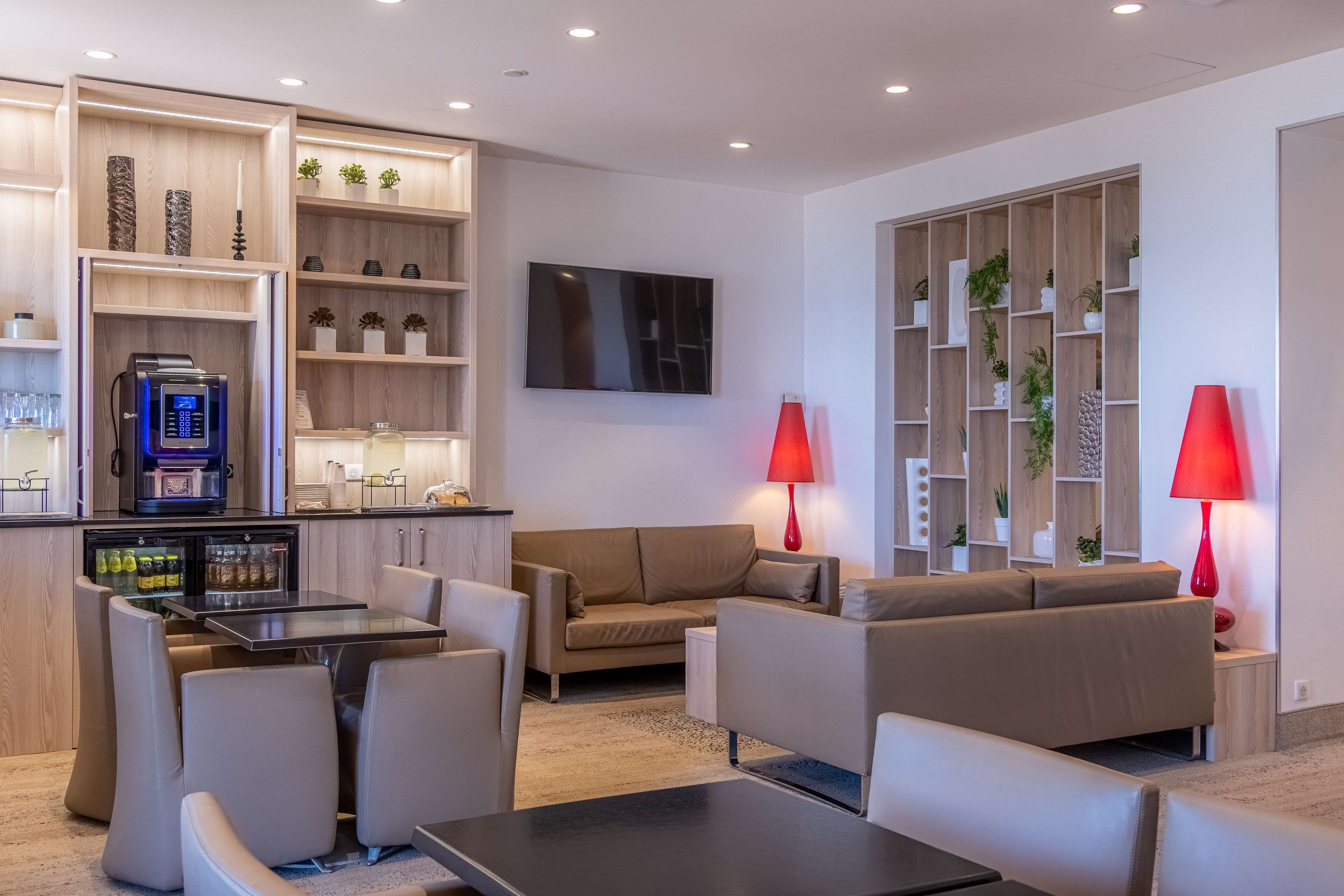 Un salon moderne avec un canapé, des fauteuils, une machine à café et un téléviseur.