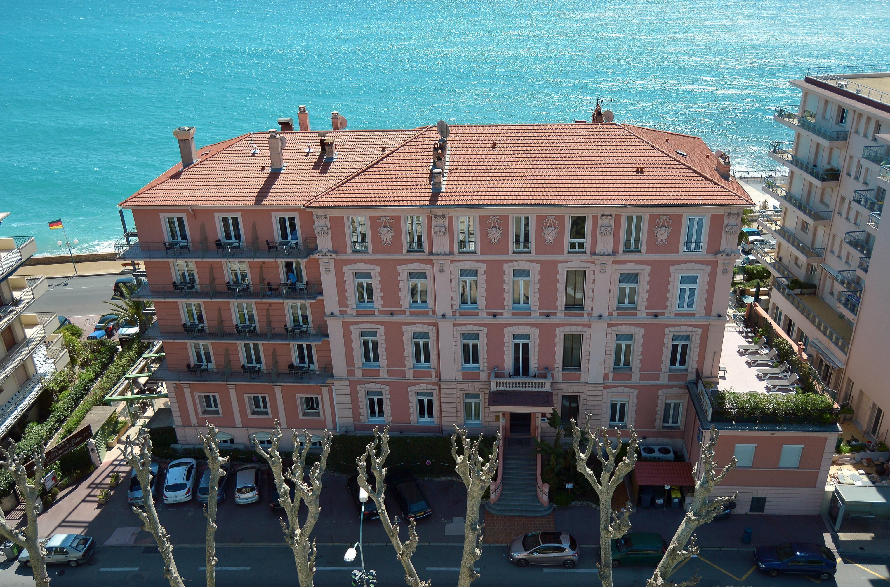 A multi-story hotel with balconies, a swimming pool, and a view of the sea.