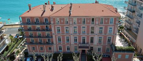 A multi-story hotel with balconies, a swimming pool, and a view of the sea.