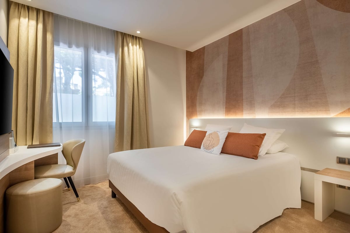 A modern hotel room with a large bed, a desk, and a chair.