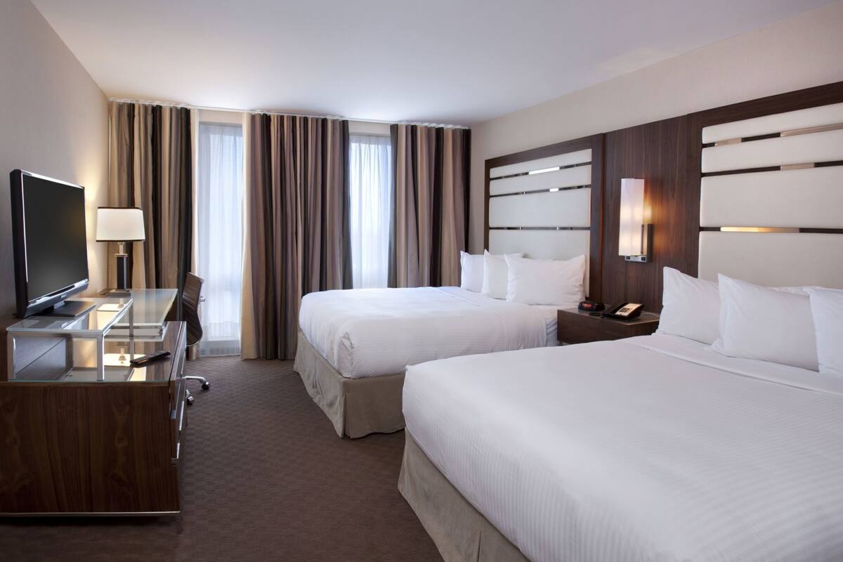 Une chambre d’hôtel avec deux lits, un bureau avec une télévision, une lampe et une table de chevet avec un téléphone.