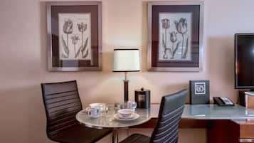 Une chambre d’hôtel dotée d’un coin repas comprenant deux reproductions botaniques encadrées, une table avec une lampe, des chaises et un téléviseur.