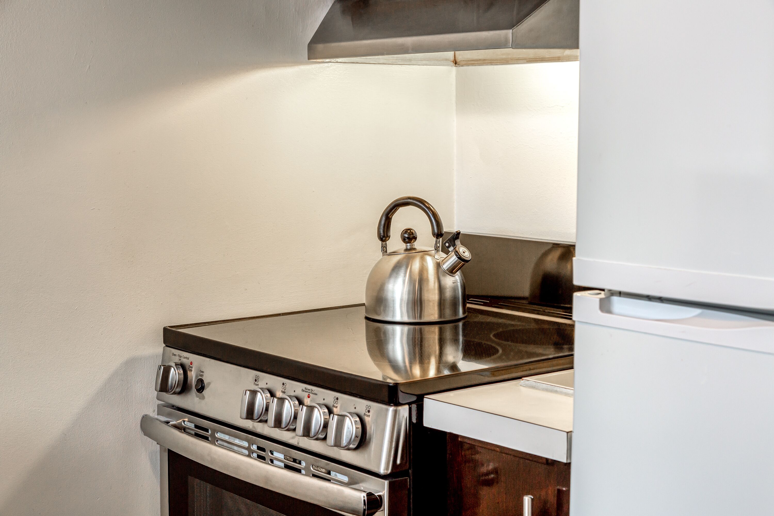 A kitchen with a stainless steel stove, a kettle, and a white refrigerator.