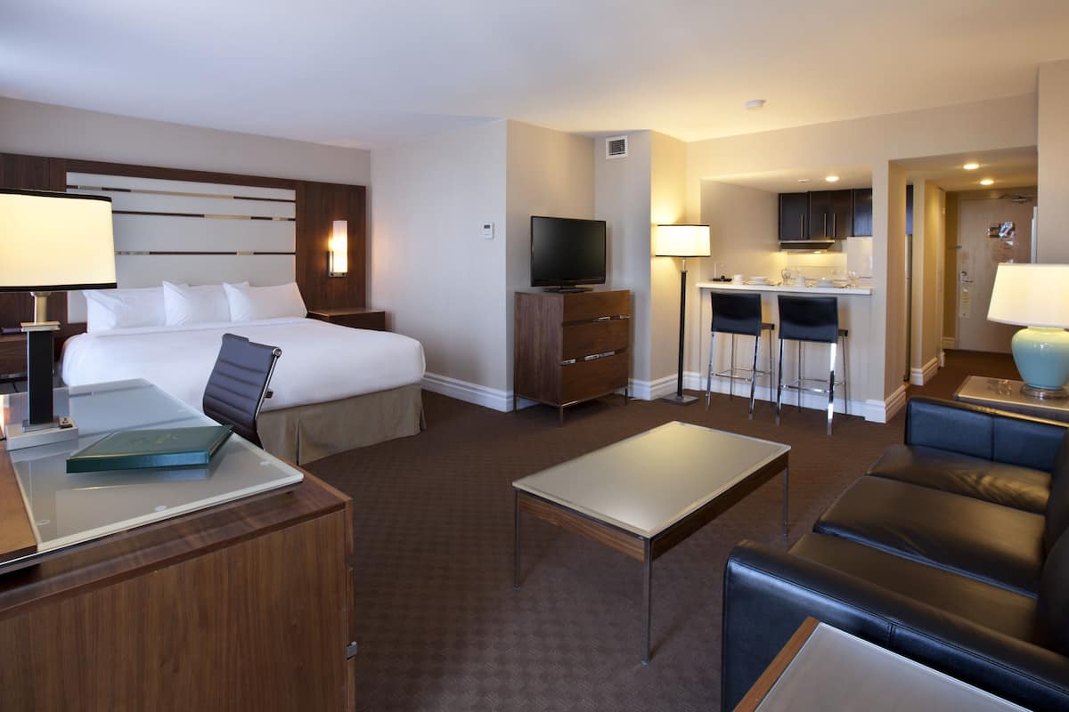 Une chambre d’hôtel comprenant un lit, un bureau, une chaise, une télévision, une kitchenette et un canapé.