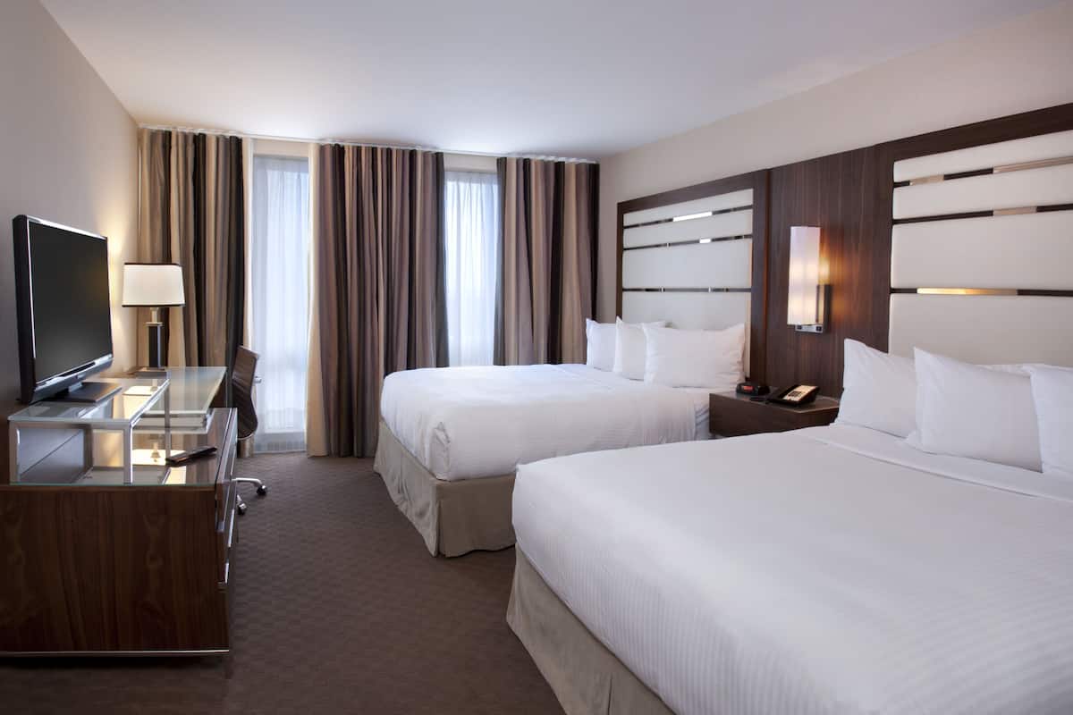 Une chambre d’hôtel avec deux lits, un bureau avec une télévision, une lampe et une table de chevet avec un téléphone.