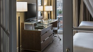 Habitación de hotel con cama, escritorio con televisor, espejo y ventana con cortinas.