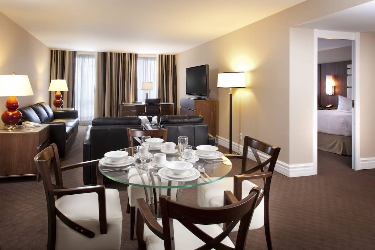 Une chambre d’hôtel comprenant un coin repas, un salon avec un canapé et une télévision, ainsi qu’une chambre à coucher séparée.