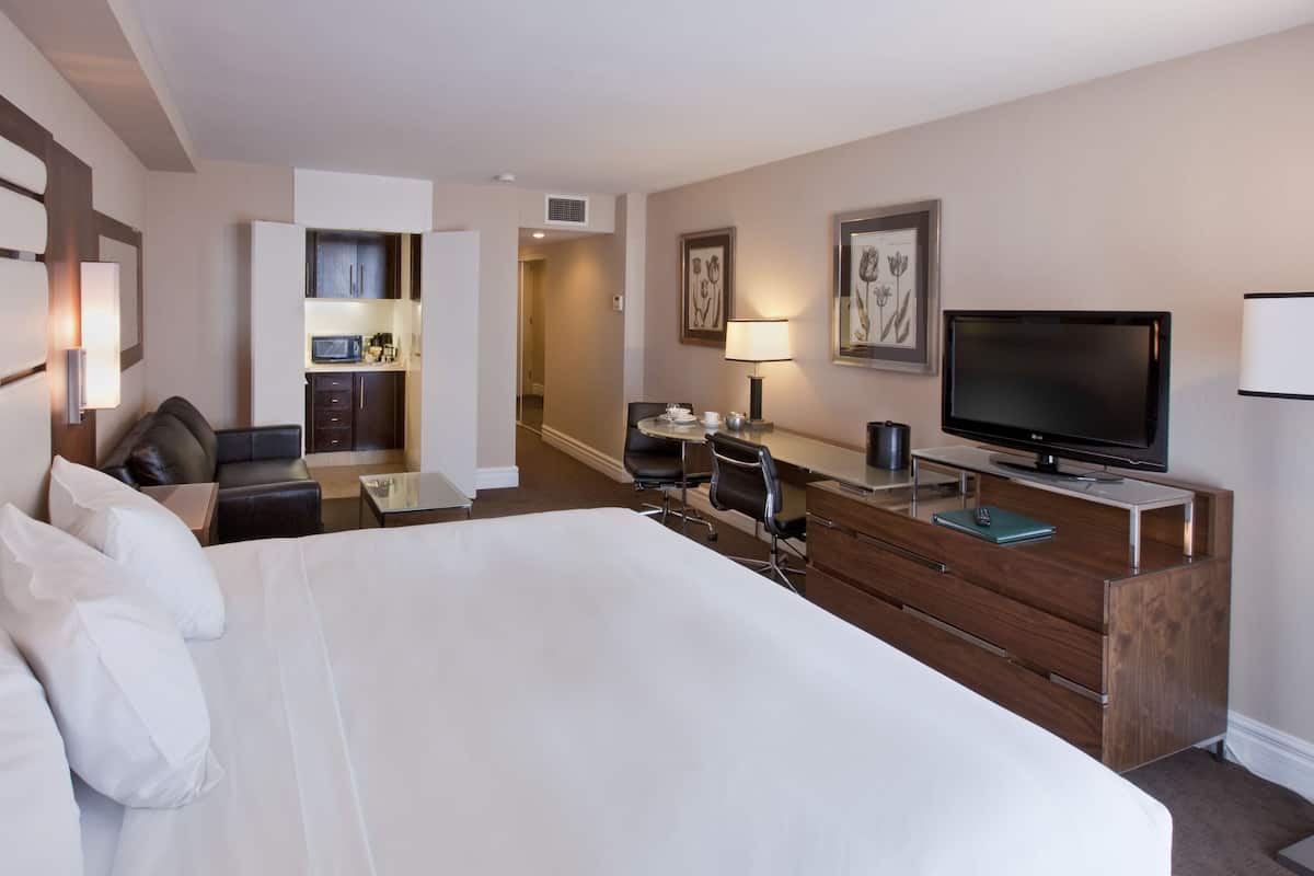 Une chambre d’hôtel avec un grand lit, un bureau avec une télévision, une kitchenette et une salle de bain.