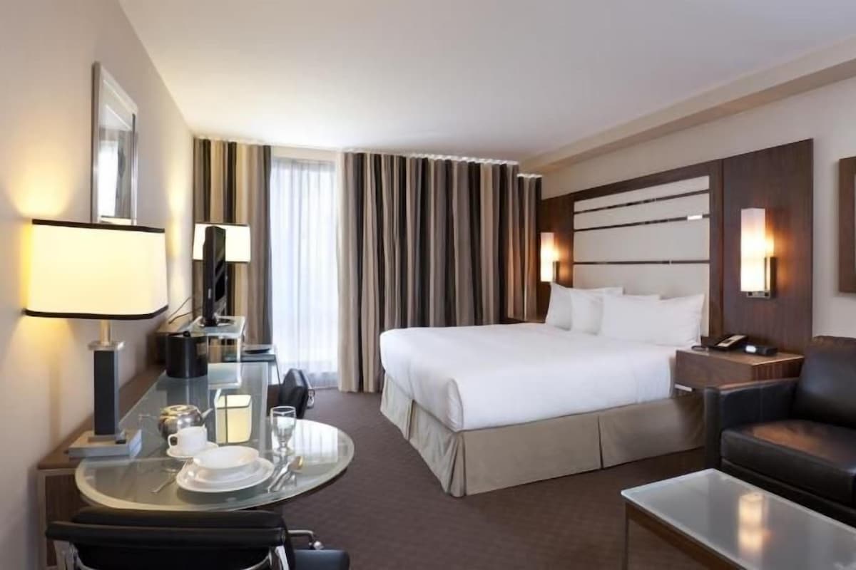 Une chambre d’hôtel comprenant un lit, un bureau avec une lampe, une table basse, un canapé et un téléviseur.
