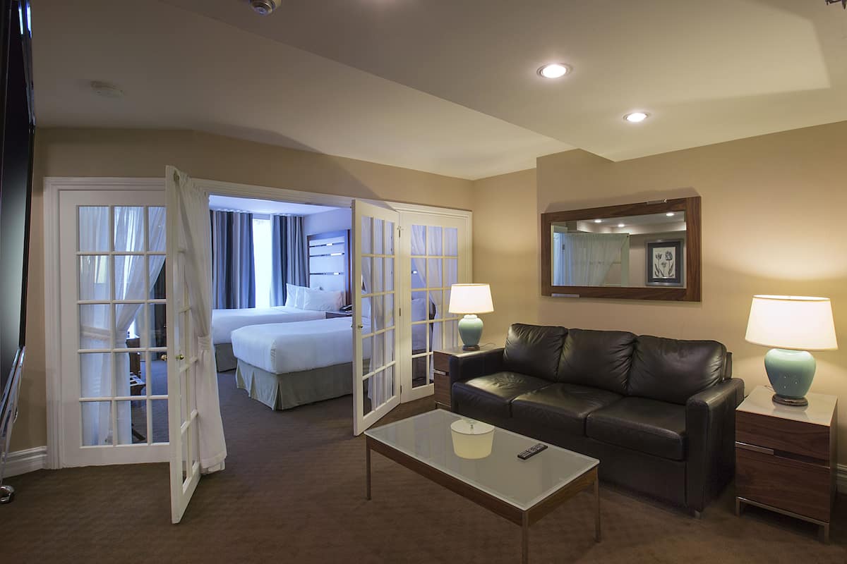 Une chambre d’hôtel comprenant un lit, un canapé en cuir, une table basse, deux tables de chevet avec des lampes et un miroir au mur.