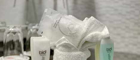 A bathroom counter with a white towel, a bottle of shower cap, and a bottle of bio shampoo.