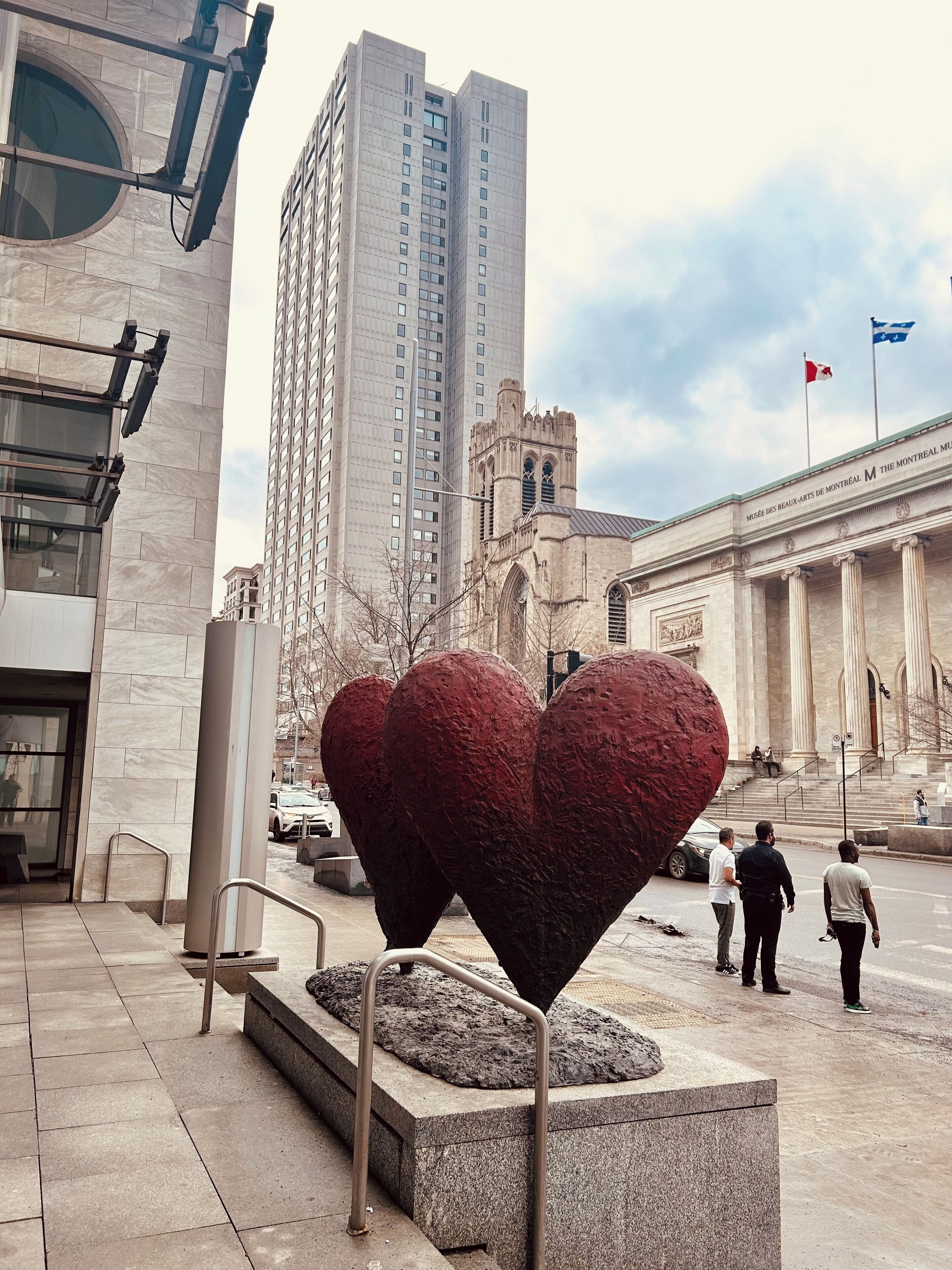 Una plaza pública con una gran escultura en forma de corazón, un edificio alto y un edificio clásico con columnas.