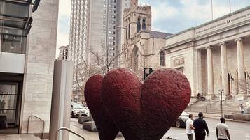 A public square with a large heart-shaped sculpture, a tall building, and a classical building with columns.
