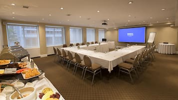 A conference room with a long table, chairs, a projector screen, and a buffet table with food and drinks.