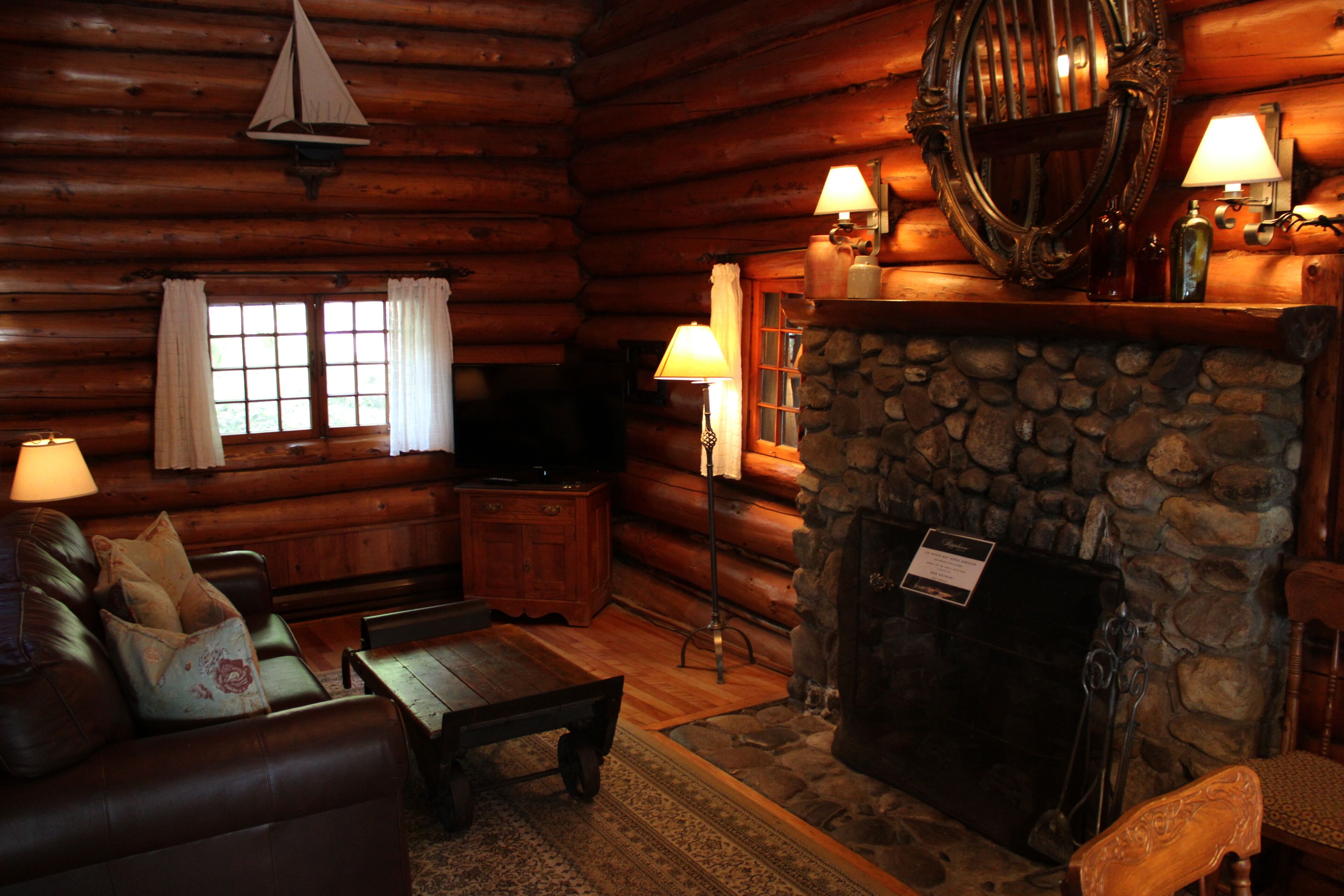 A log cabin interior with a stone fireplace, leather furniture, and a wooden ceiling.