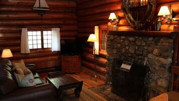 A log cabin interior with a stone fireplace, leather furniture, and a wooden ceiling.