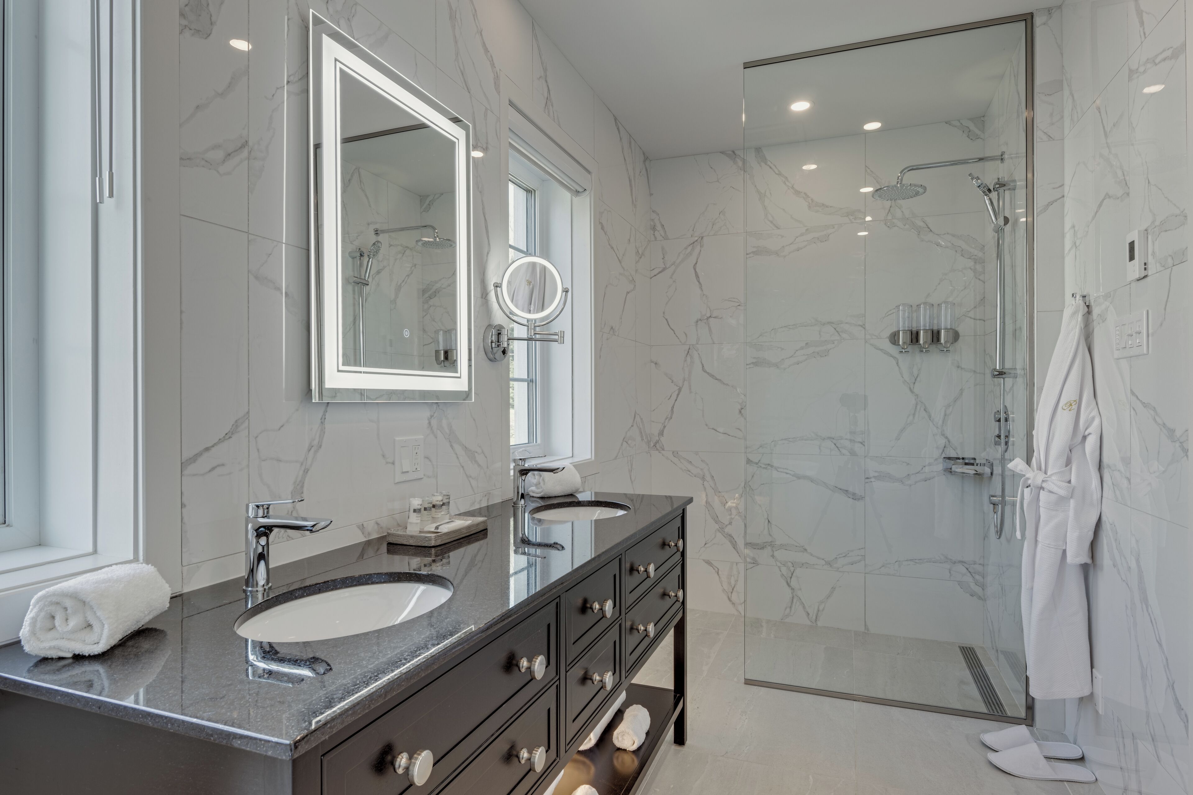 A modern bathroom with two sinks, a large mirror, and a glass-enclosed shower.