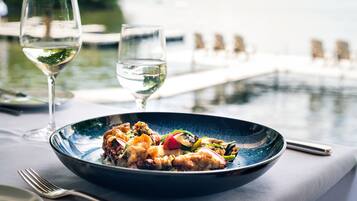 Una mesa de comedor con un plato de comida azul, dos copas de vino y vista a un cuerpo de agua.