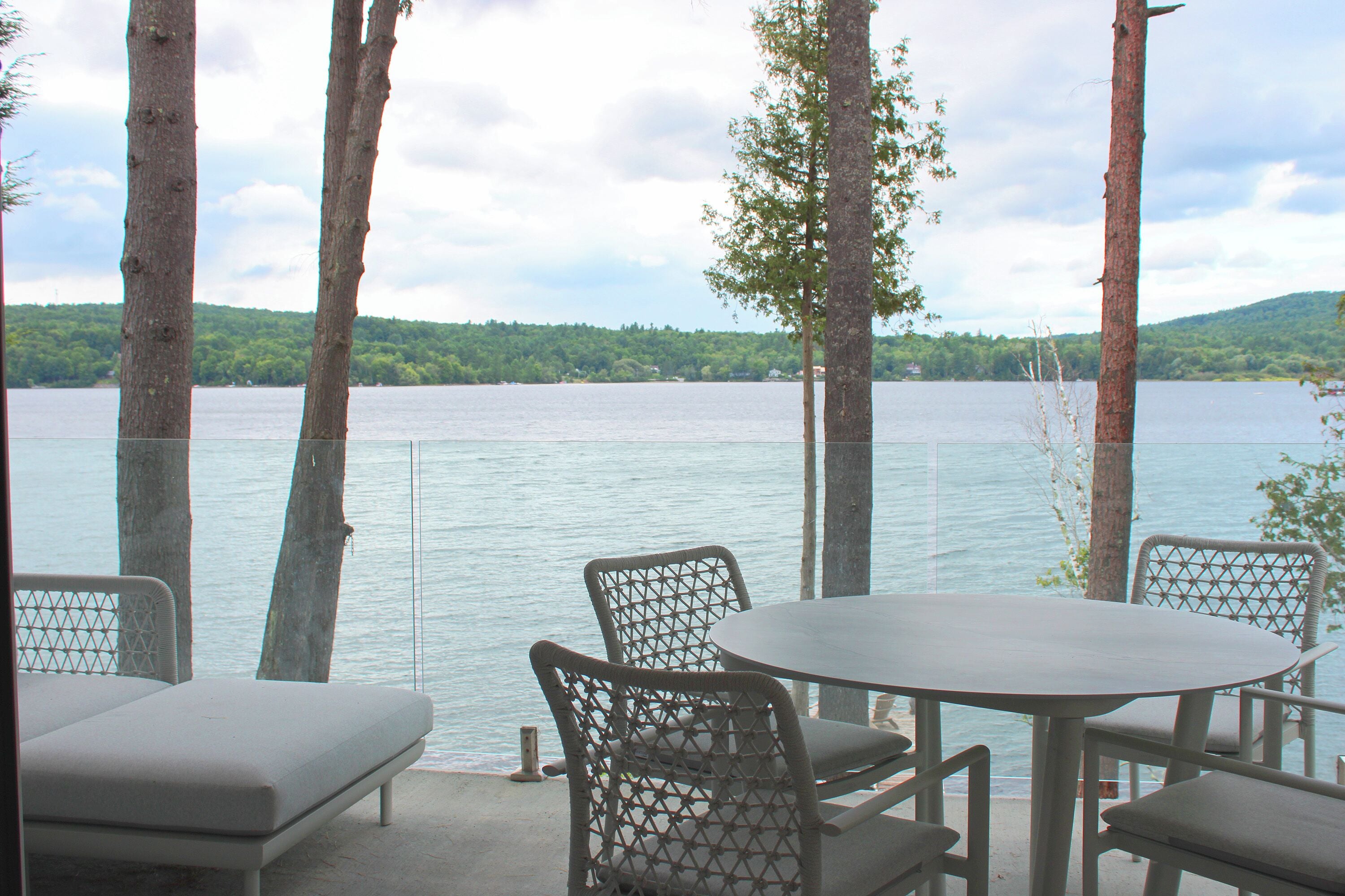 Een terras met een tafel en stoelen met uitzicht op een meer, omringd door bomen.