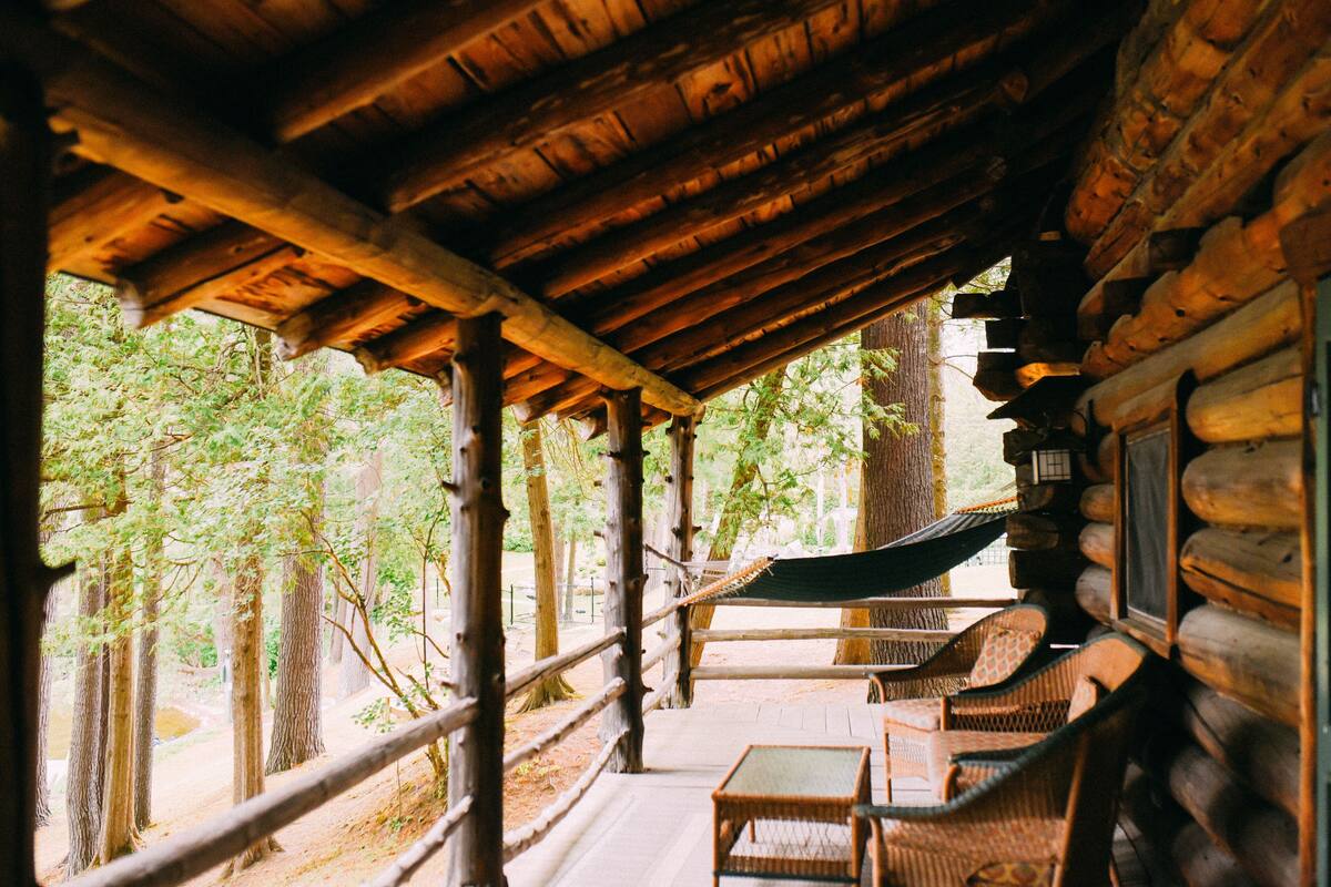 A wooden cabin with a porch, wicker furniture, and a view of the forest.