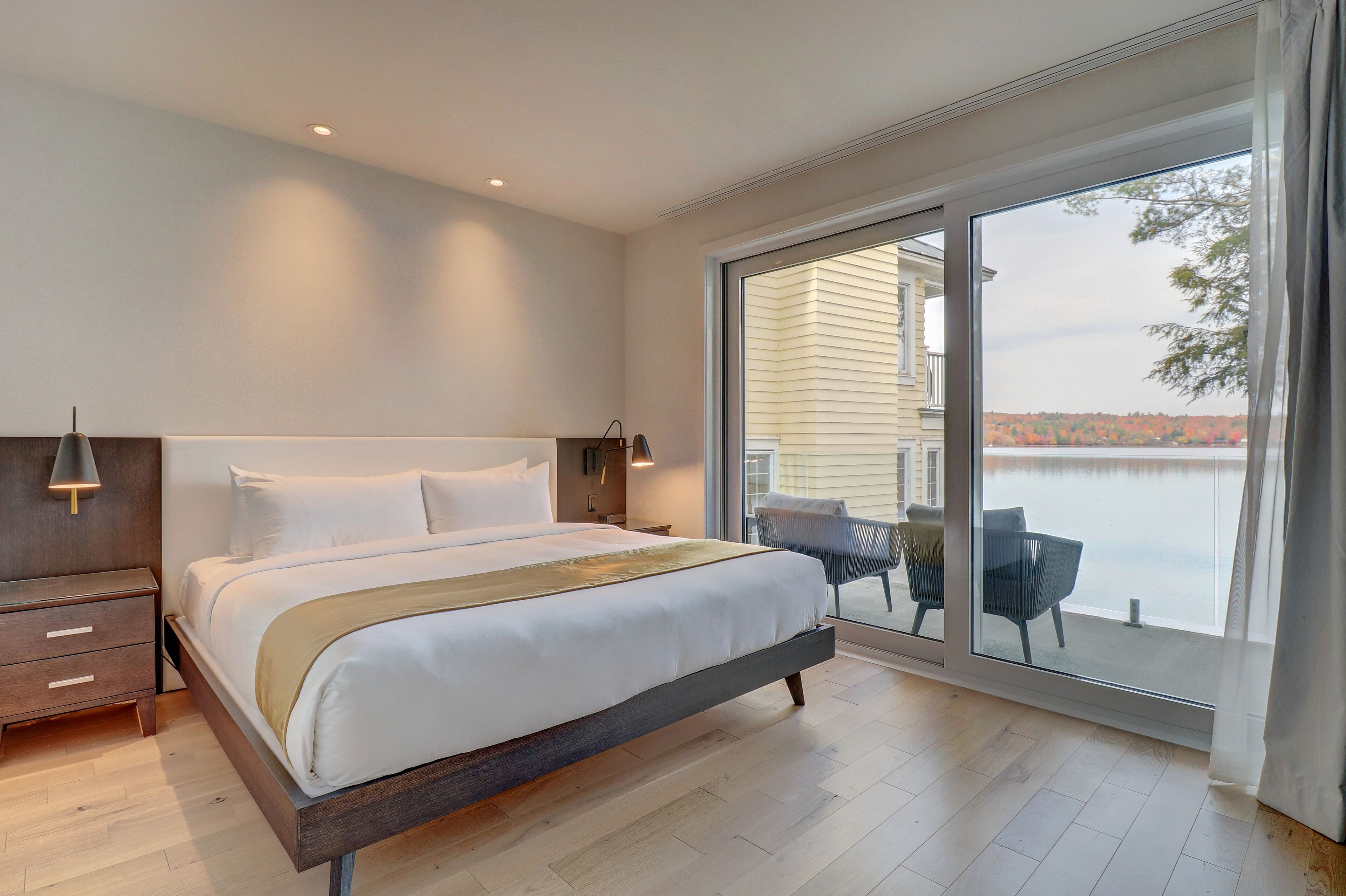 Une chambre moderne avec un grand lit, une table de chevet, une chaise et une vue sur un plan d’eau, visible à travers une porte-fenêtre coulissante.