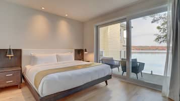 Une chambre moderne avec un grand lit, une table de chevet, une chaise et une vue sur un plan d’eau, visible à travers une porte-fenêtre coulissante.