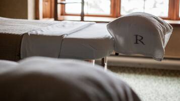 A room with a bed, a pillow with a letter 'R', and a window with natural light.
