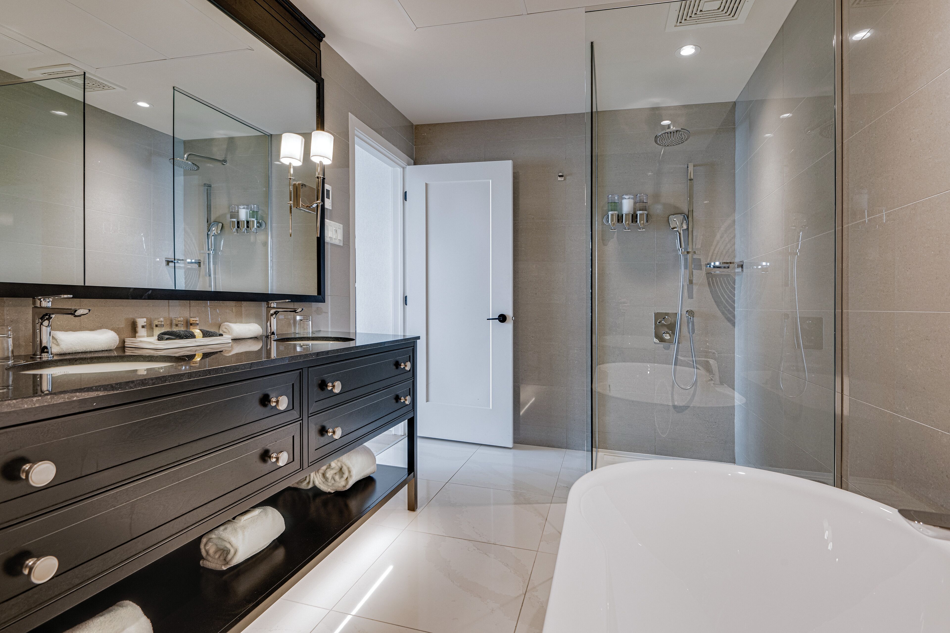 A modern bathroom with a glass-enclosed shower, a large mirror, and a bathtub.