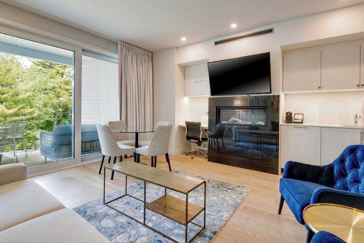A modern living room with a sofa, chairs, a coffee table, a fireplace, and a TV.