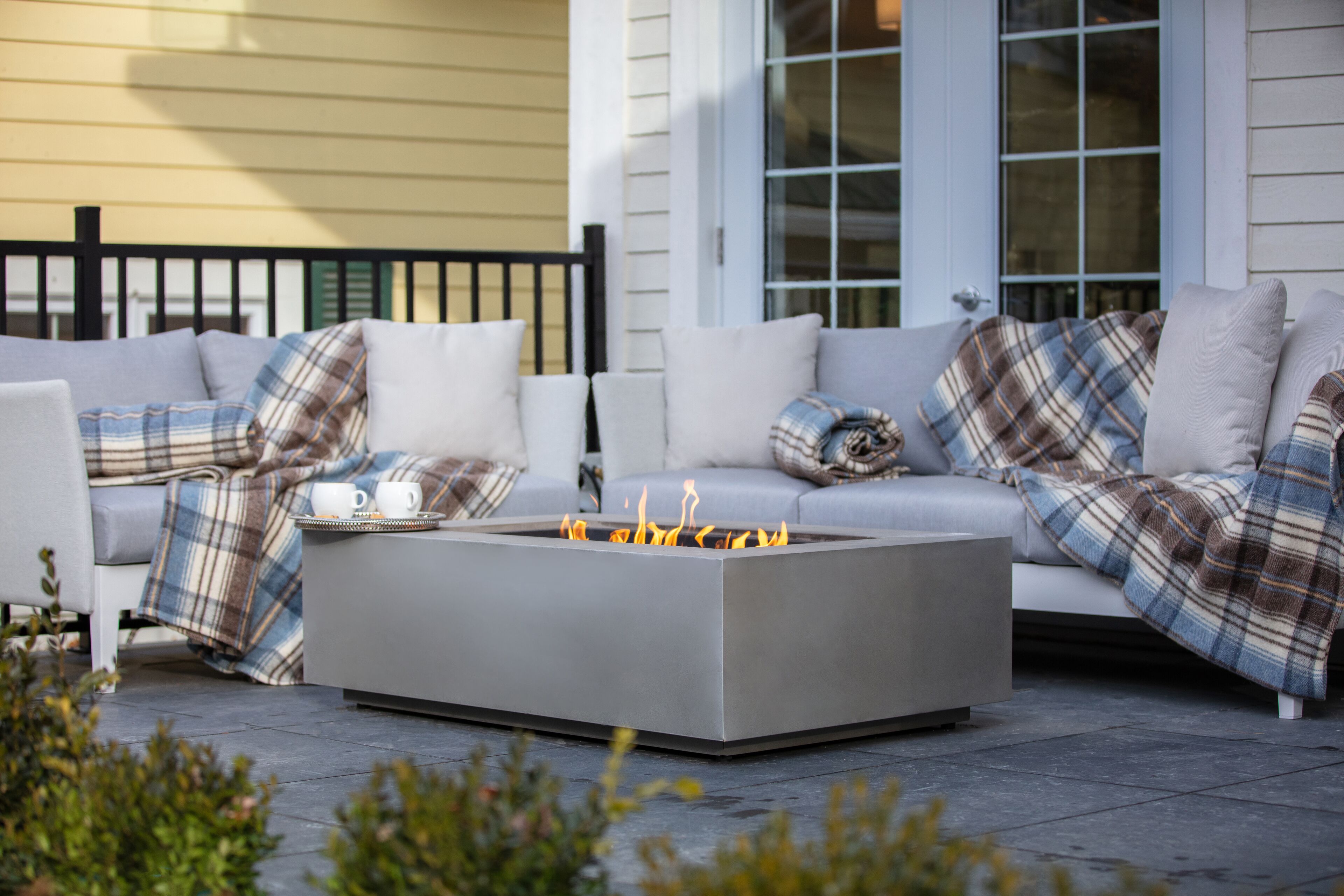 A modern outdoor seating area with a fire pit table, cushioned sofas, and a bench.