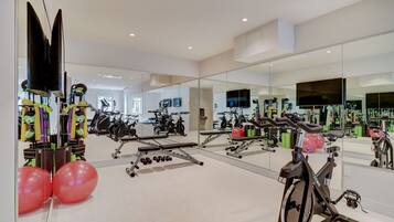 A modern gym with exercise equipment, mirrors, and a large TV.
