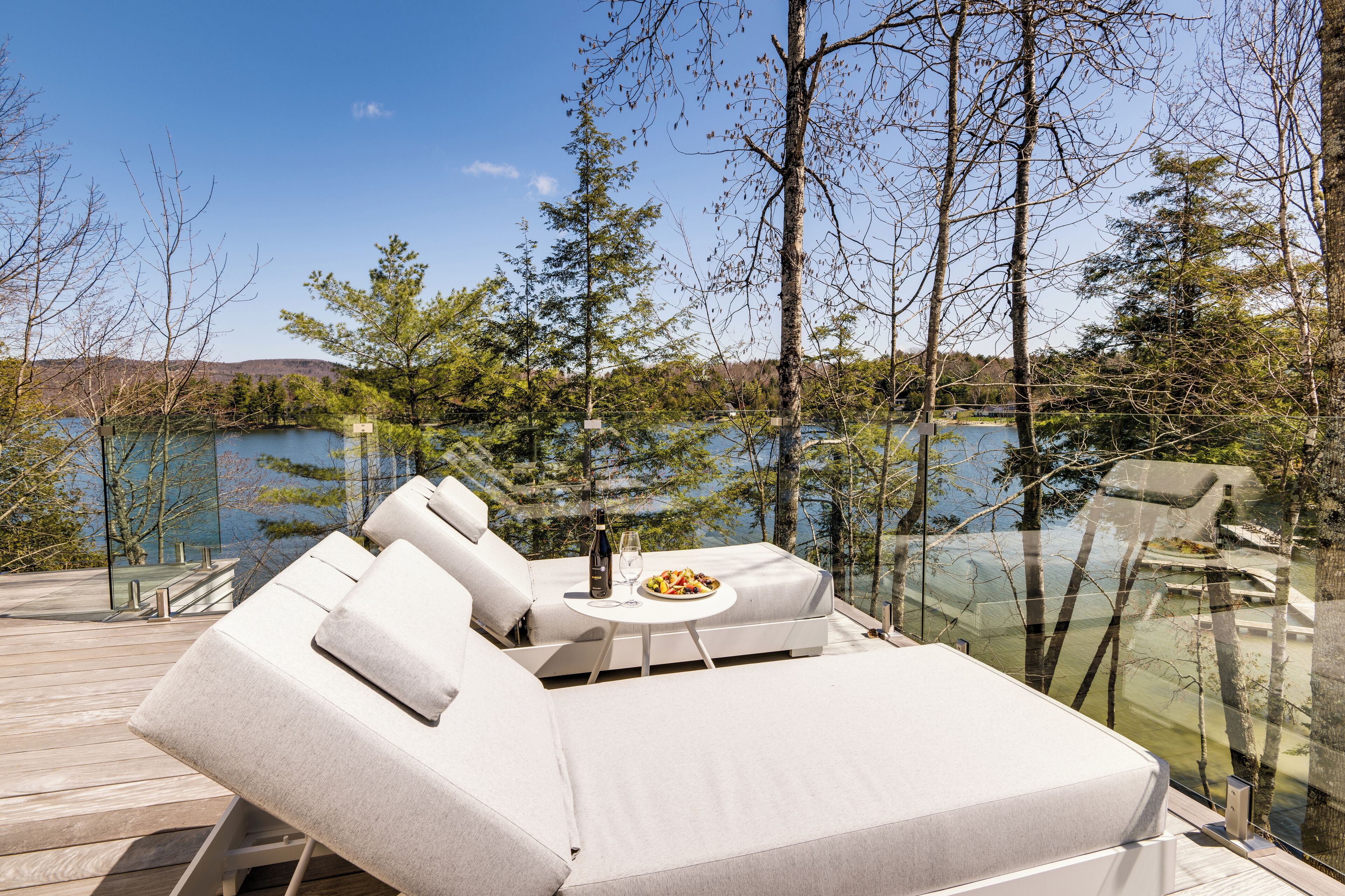 Une terrasse avec un canapé et une table, donnant sur un lac bordé d’arbres et sur un bâtiment situé au loin.