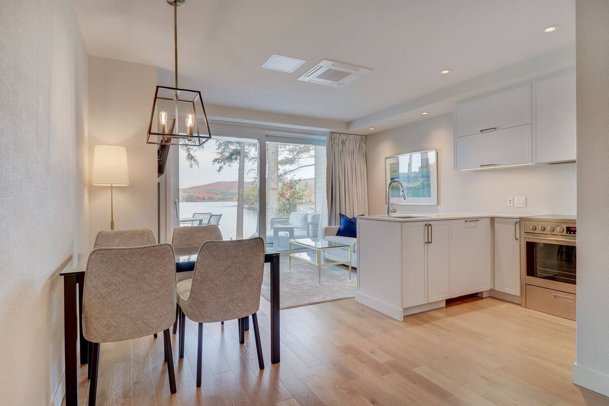 A modern kitchen with white cabinets, a built-in oven, and a dining area with a table and chairs.