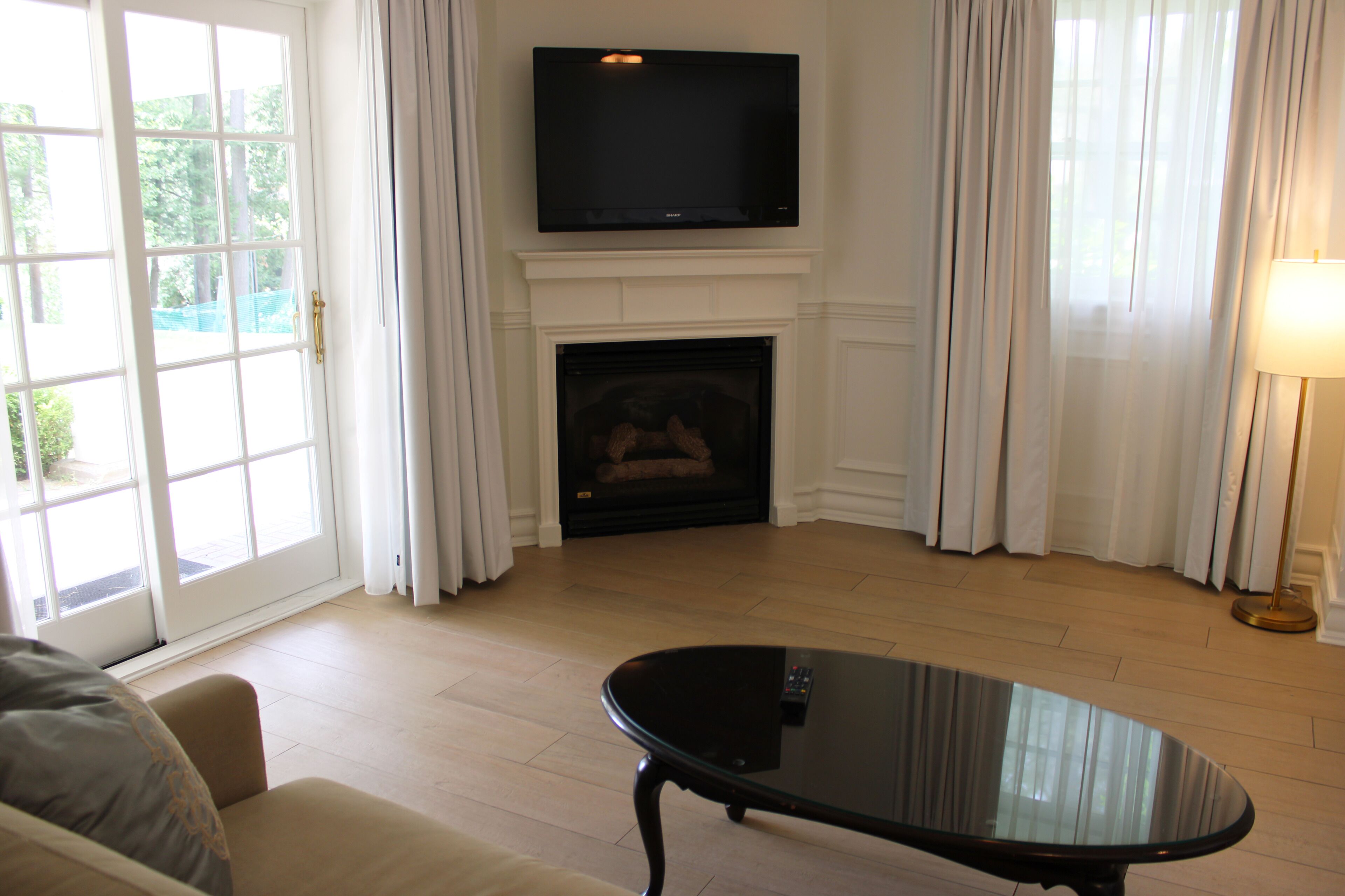 A living room with a fireplace, a television mounted above it, and a glass coffee table.