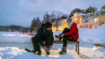 Two people sitting on a bench in a snowy outdoor area with a body of water and buildings in the background.