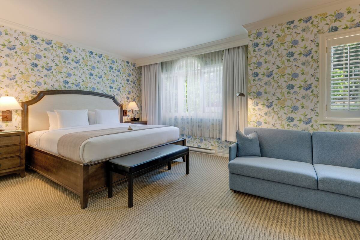 A bedroom with a bed, bedside tables, a bench, a sofa, and floral wallpaper.