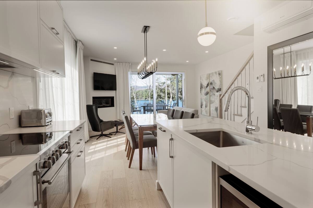 A modern kitchen with a central island, built-in oven, and a dining area with chairs and a table.