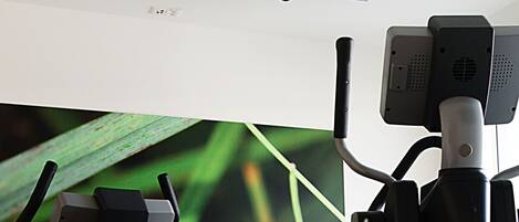 A gym with stationary bikes, a treadmill, and a small table with water bottles and fruit.