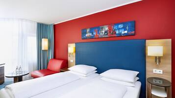 Ein Hotelzimmer mit einem großen Bett, einem roten Sessel, einem kleinen Tisch mit Lampe und einem Bild an der Wand.