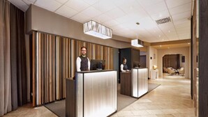 Ein Hotel-Empfangsbereich mit zwei Angestellten an der Rezeption, einem modernen Design mit gestreifter Wand und einer geräumigen Lobby mit Sitzgelegenheiten.