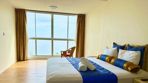 A hotel room with a large bed, a chair, and a view of the sea through a large window. - Acacia Court Hotel (Cairns North)