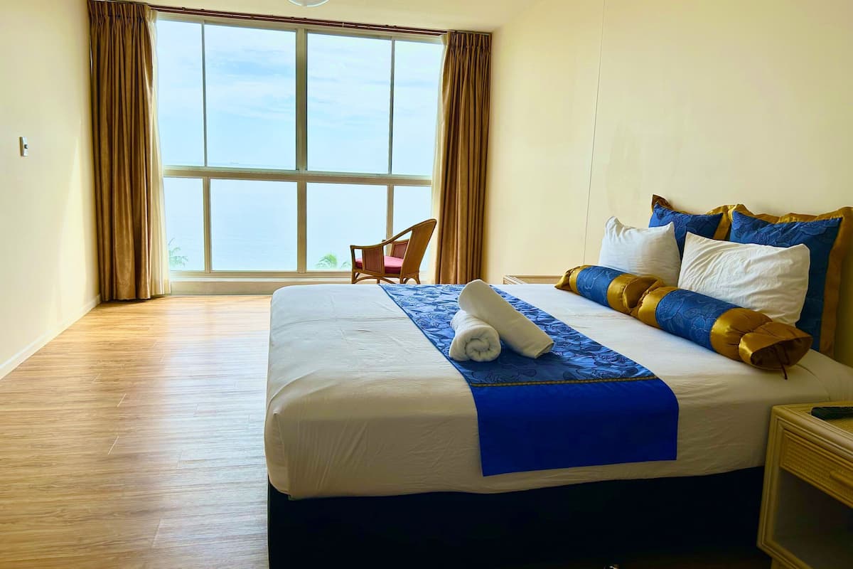 A hotel room with a large bed, a chair, and a view of the sea through a large window.