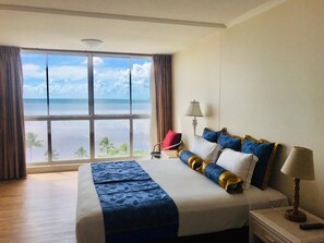 A hotel room with a large window offering a view of the ocean and palm trees. - Acacia Court Hotel (Cairns North)