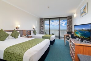 A hotel room with two beds, a desk with a computer, a television, and a balcony with a view of the sea. - Acacia Court Hotel (Cairns North)