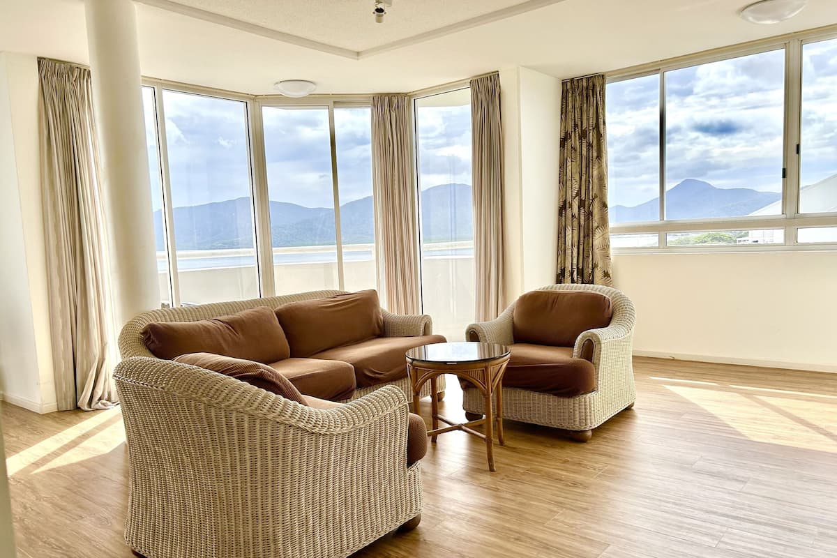 A spacious room with a large window offering a mountain view, a brown sofa, a brown armchair, and a small round table.