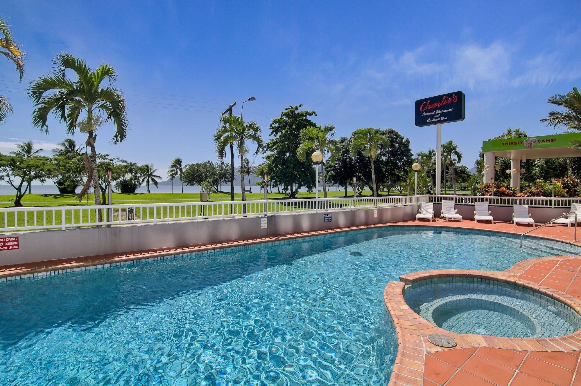 Una piscina con hidromasaje, rodeada de palmeras y vista al océano.