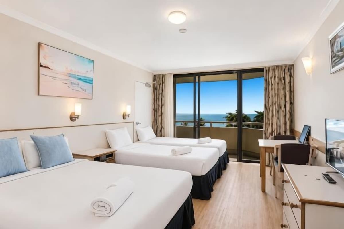 A hotel room with two beds, a desk, a chair, and a large window with a view.